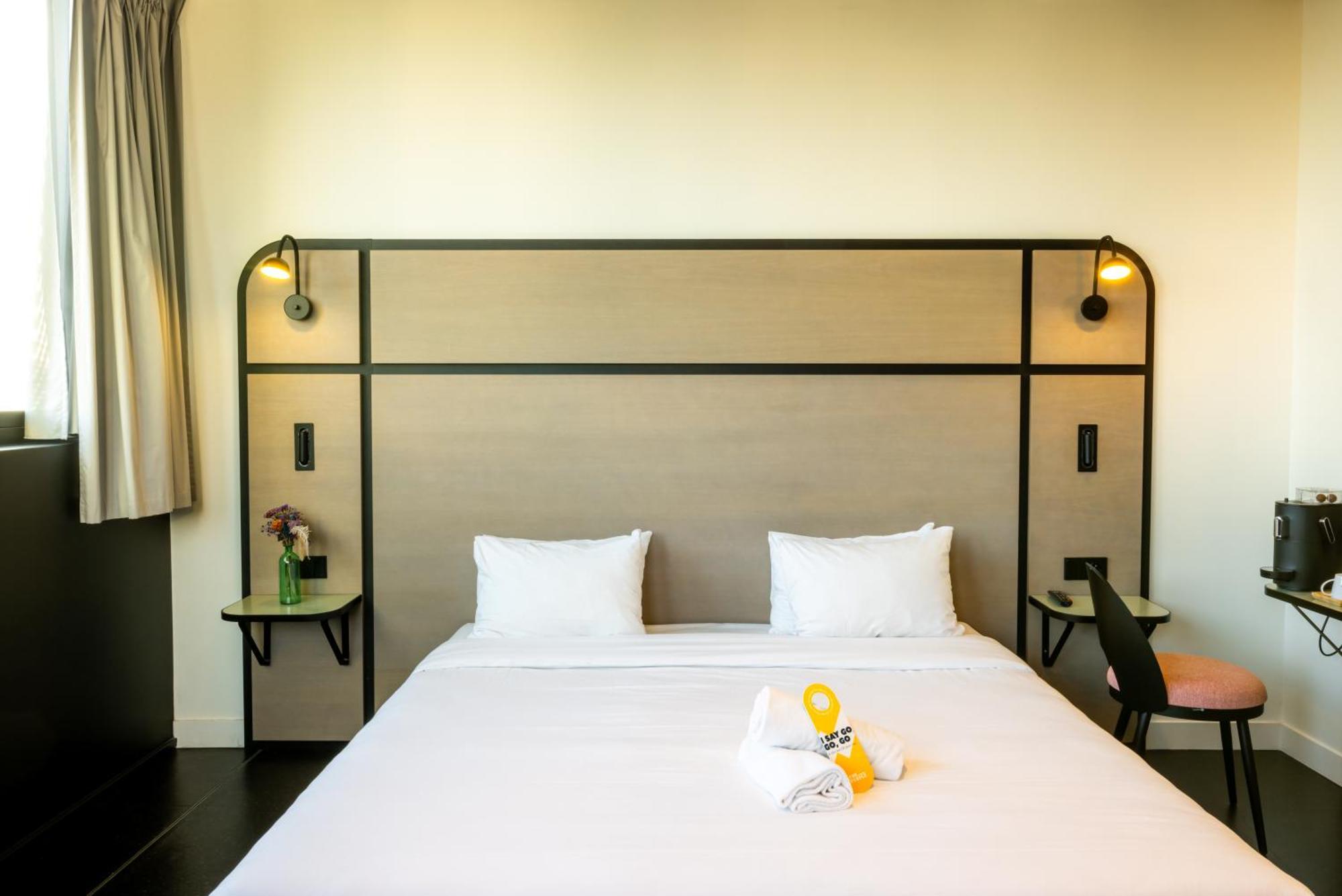 Auberge de jeunesse The People - Paris Marais Extérieur photo The photo shows a modern hotel room setup featuring a double bed with a simple white duvet and two white pillows. The headboard is designed with a light wooden finish and framed by black accents, complemented by stylish wall sconces on either side. S